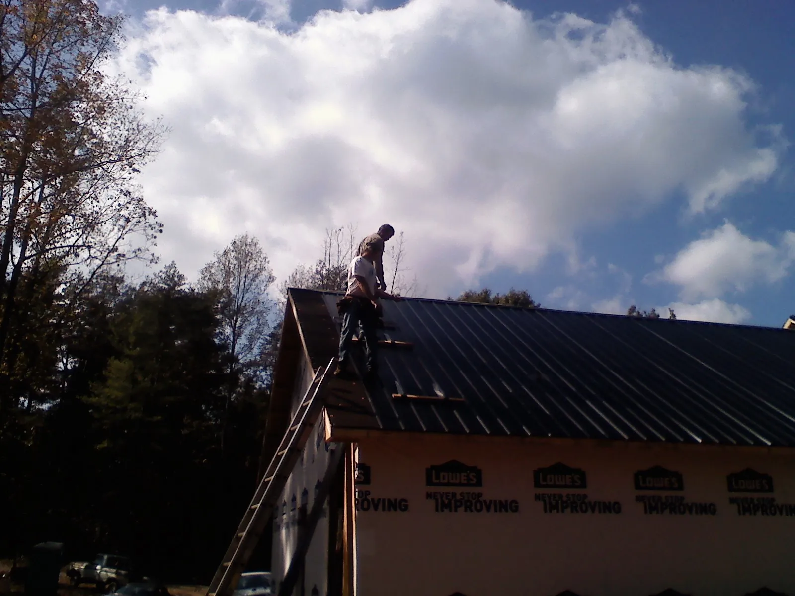 Roofer fastening dark metal panels high against a cloudy sky, from a Roof Inspection job in Blacksburg