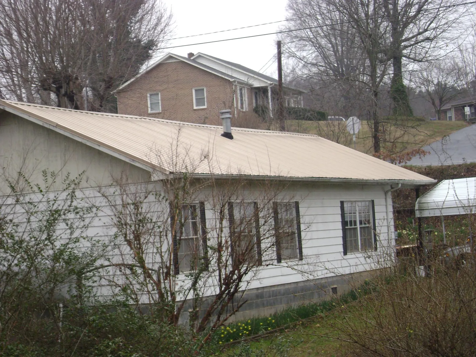 Tan metal roof on a white sided house set into a hillside — Commercial Roofing by Roofing Brothers in Blacksburg